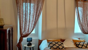 Un dormitorio con cama, cortinas, una mesita de noche con lámpara, alfombra y armario de madera.