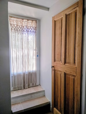 Eine Holztür mit einem Metallgriff, eine Treppe aus Beton, die zu einem Fenster mit einem gemusterten Vorhang führt.