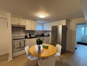 A modern kitchen with white cabinets, stainless steel appliances, and a wooden dining table. - Cozy Bright Suite with Separate Entrance in Scarborough | Near Hospital (Toronto)