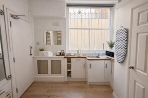 A compact kitchen with white cabinetry, a window with a view, a microwave, and a sink. - Apartment 3 min Tube West Kensington (London)
