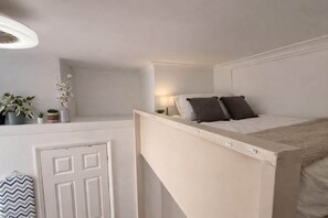 Ein Schlafzimmer mit Etagenbett, Nachttisch mit Lampe, einer Tür und einer Topfpflanze auf einem Regal.