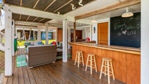 A covered outdoor seating area with a bar, wooden stools, and a chalkboard with a welcome message. - Welcome to Waters Edge, a true hidden gem on Little Gasparilla Island-where turquoise water, gentle breezes, and total relaxation replace traffic, noise, and stress (Placida)