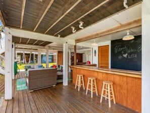 Ein überdachter Außenbereich mit Sitzgelegenheiten, einer Bar, Holzstühlen und einer Tafel mit einer Willkommensbotschaft.