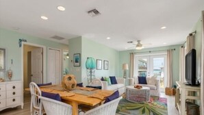 A dining area with a wooden table and chairs, a sofa, a television, and a view of the sea through a glass door. - Welcome to Waters Edge, a true hidden gem on Little Gasparilla Island-where turquoise water, gentle breezes, and total relaxation replace traffic, noise, and stress (Placida)