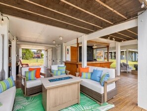 Un espace extérieur aménagé, abrité et doté de mobilier en osier, d’un bar en bois et offrant une vue sur le paysage.