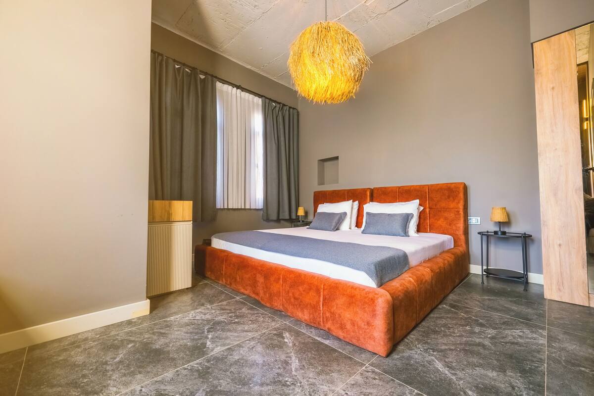Ein modernes Schlafzimmer mit einem großen Bett, einer Pendelleuchte und Blick ins Freie.