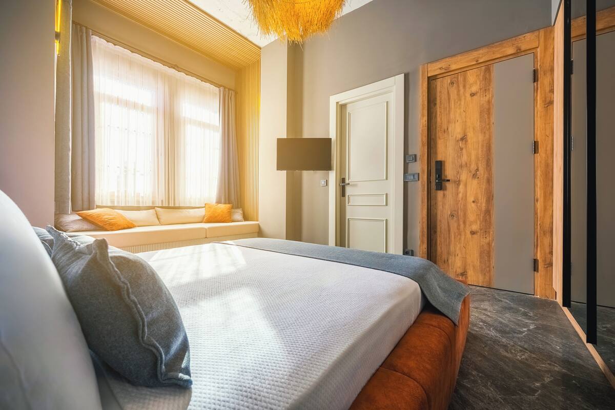 Ein Schlafzimmer mit einem Bett, einem Fenster mit Vorhängen, einer Holztür und einer Wandleuchte.