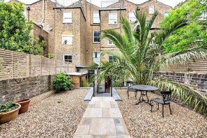 A courtyard with a gravel path, a table and chairs, and a palm tree. - Stylish Notting Hill Apartment (Greater London)