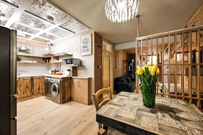 A modern kitchen with wooden cabinets, a dishwasher, and a dining area with a table and chairs. - Stylish Notting Hill Apartment (Greater London)