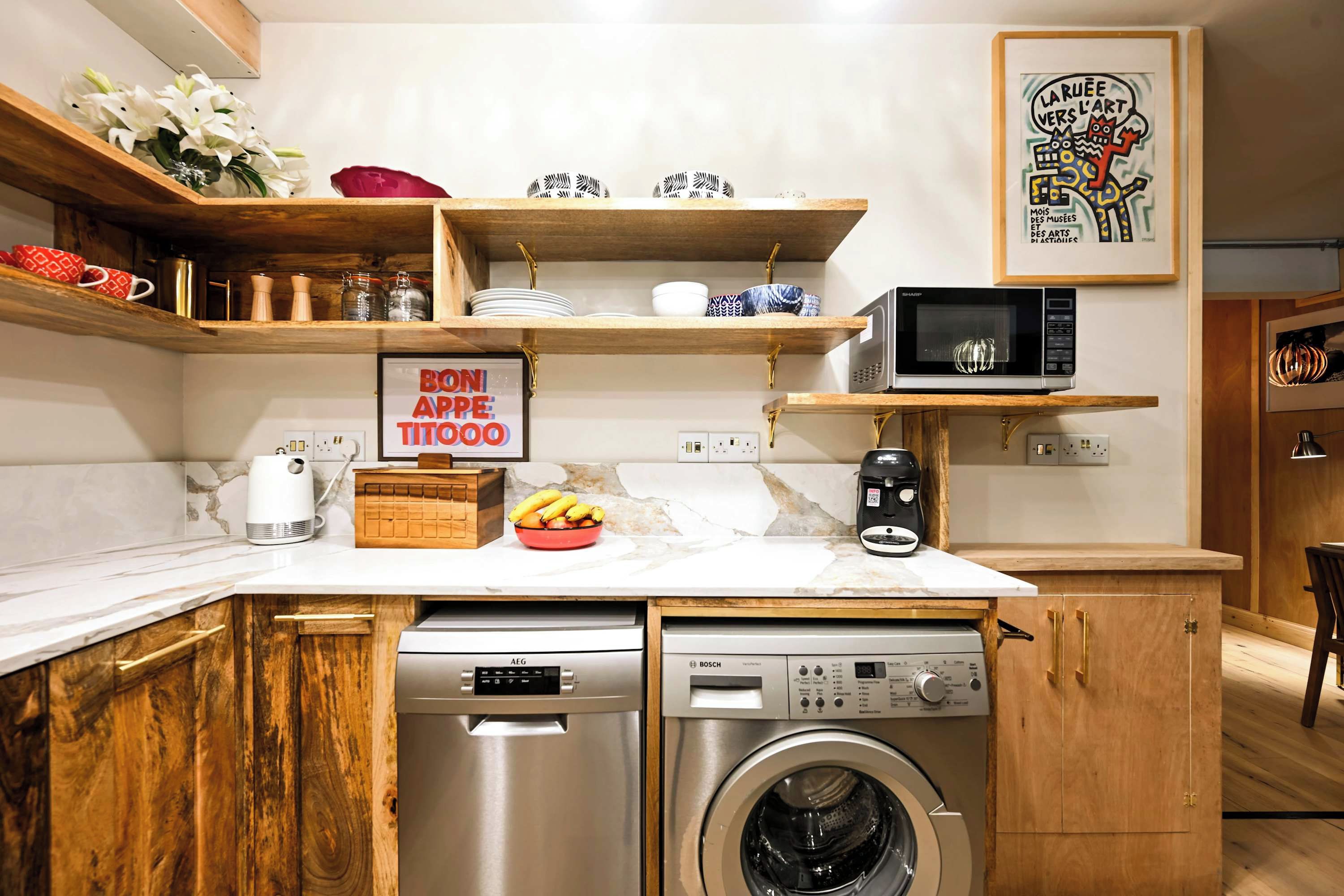 A compact kitchen with wooden cabinets, a dishwasher, a washing machine, and a microwave.