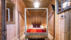Ein hölzernes Himmelbett mit einer rot-orange karierten Tagesdecke, zwei Nachttischlampen und einer Holzzieldecke mit einer modernen Leuchte.