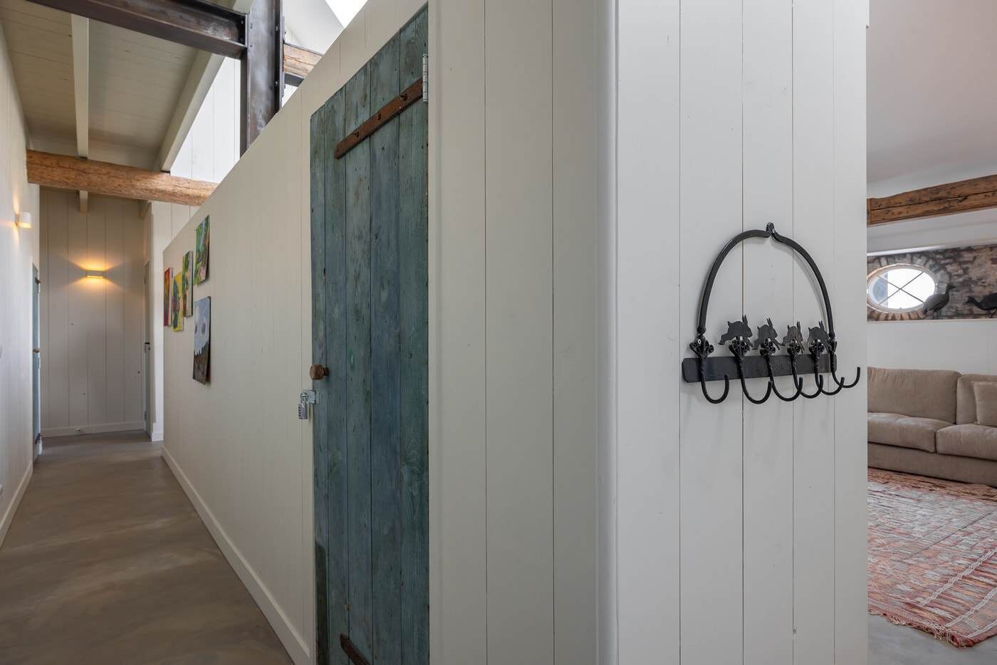 A hallway with a wooden door, a coat rack with hooks, and a couch in the adjacent room.