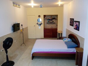 A bedroom with a bed, a bedside table, a fan, a dresser, a mirror, and a shelf with books and decorations. - Studio apartment - apartment in the neighborhood outside the historic district (cartagena)