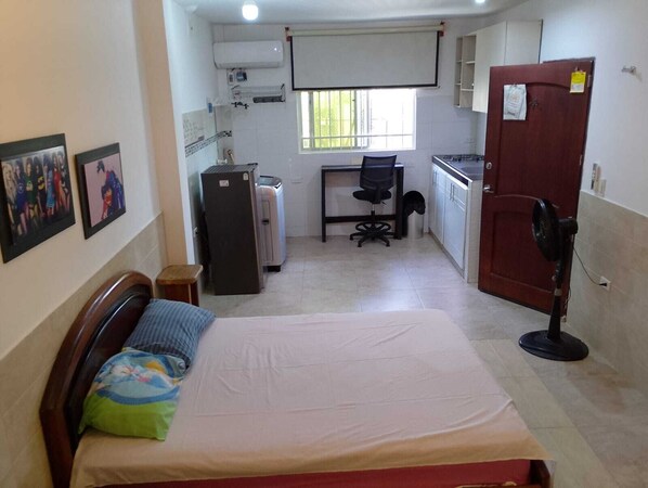A small, compact room with a bed, a desk, a refrigerator, a fan, and a window. - Studio apartment - apartment in the neighborhood outside the historic district (cartagena)