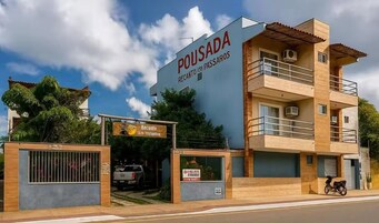 Um edifício com uma placa que diz 'POUSADA RECANTO 135 PASSAROS' e uma entrada com portão.
