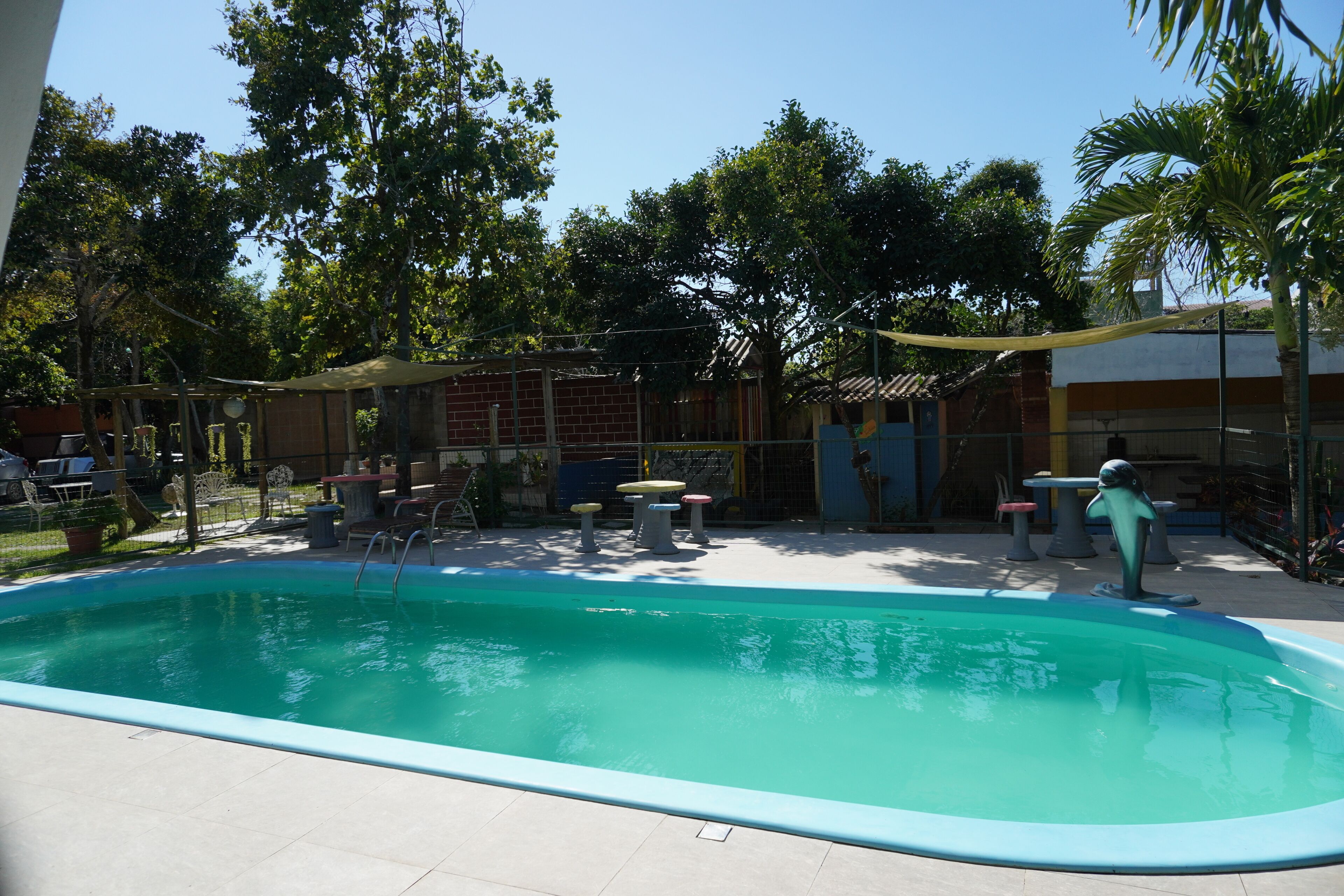 A swimming pool with a tiled deck, surrounded by outdoor furniture and trees.