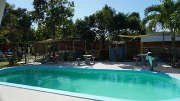 A swimming pool with a tiled deck, surrounded by outdoor furniture and trees.