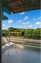 Uma varanda com uma cadeira, vista para uma estrada e vegetação.