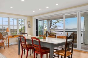A dining area with a large table, chairs, and a view through glass doors.