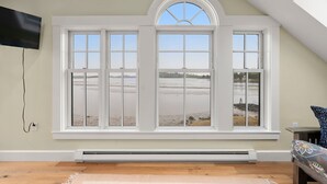 Una habitación con un amplio ventanal con vista a la playa, un televisor de pantalla plana montado en la pared y un calentador integrado.