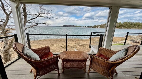 A covered outdoor seating area with wicker furniture and a view of a lake.