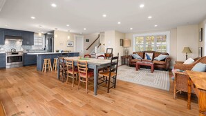 A spacious kitchen with wooden flooring, a dining area with a table and chairs, a living room with a sofa and a coffee table, and a staircase leading to another level. - Robbin's Nest - Panoramic Essex Bay Waterviews (Essex)