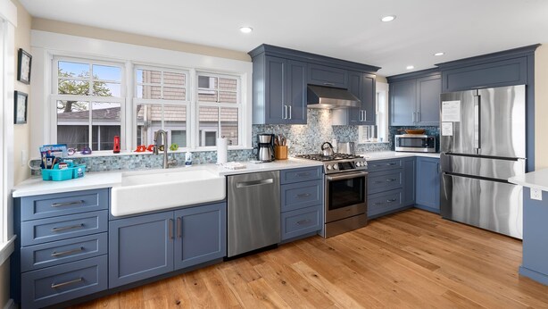 A modern kitchen with blue cabinets, stainless steel appliances, and a large window. - Robbin's Nest - Panoramic Essex Bay Waterviews (Essex)