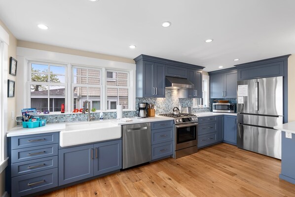 A modern kitchen with blue cabinets, stainless steel appliances, and a large window. - Robbin's Nest - Panoramic Essex Bay Waterviews (Essex)