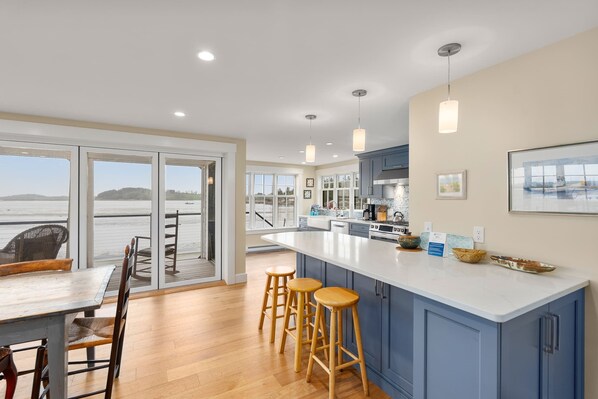 A modern kitchen with a large island, bar stools, and a view of the water. - Robbin's Nest - Panoramic Essex Bay Waterviews (Essex)