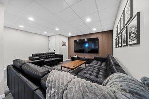 Un salon moderne doté d’un grand téléviseur à écran plat, de canapés en cuir noir, d’une table basse en bois et de tableaux encadrés accrochés au mur.