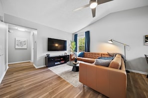 A modern living room with a sofa, TV, and ceiling fan.