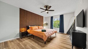 A modern bedroom with a bed, a ceiling fan, a nightstand, a dresser, and a TV.