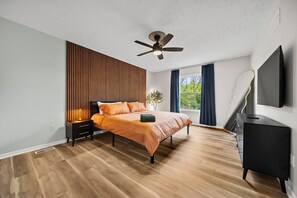 Une chambre à coucher moderne, équipée d’un lit, d’un ventilateur de plafond, d’une table de chevet, d’une commode et d’un téléviseur.