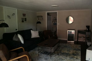 A living room with a black sofa, a wooden coffee table, a brown armchair, a small round mirror, and a white cabinet.