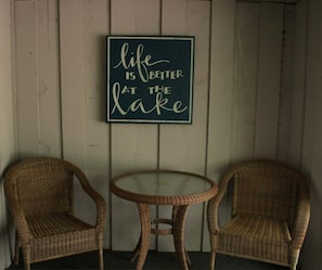 Two wicker chairs and a small table against a wooden wall with a motivational quote.