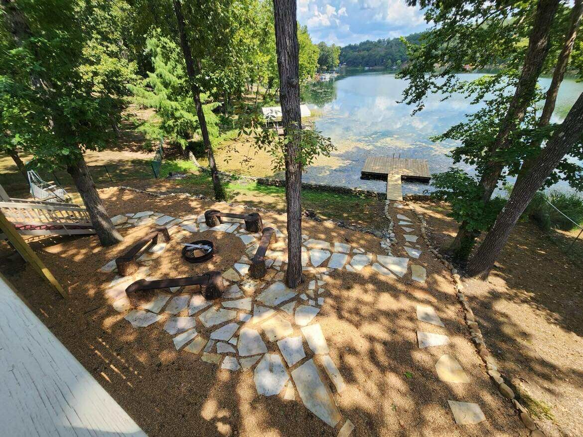 A lakeside patio with stone flooring, a hammock, and a fire pit.