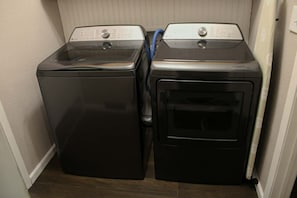 Two stacked front-loading washers in a laundry room with a wooden floor and a white wall.