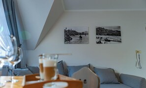 Ein Zimmer mit Esstisch, einem Bierglas, einer Couch und zwei schwarz-weißen Fotos an der Wand.