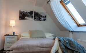 Ein Schlafzimmer mit Bett, Nachttisch, Lampe, einem Fenster mit Bergblick und zwei Wandbildern.