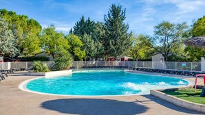 Uma piscina com um deck ao redor, árvores e uma cerca.