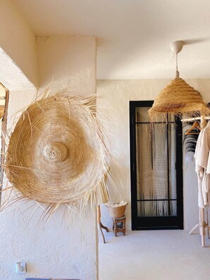 Una stanza con un grande cesto di vimini, un oggetto decorativo appeso, una finestra con cornice nera e uno sgabello.