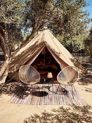 A tent with two wicker chairs and a small table, set on a striped mat.