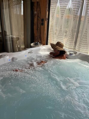 A hot tub with a person wearing a straw hat, surrounded by wooden decor and a patterned curtain. - Domaine de la Finca Lessya Lodges & SPA, Tipi Bohème - Aventure Insolites (Mauguio)