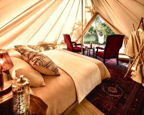 Quarto em formato de tenda com uma cama, cadeiras vermelhas, uma mesa e um cabideiro.