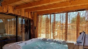 Una vasca idromassaggio in una baita di legno con una finestra che si affaccia sugli alberi.