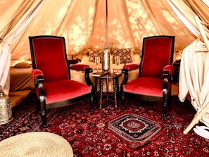 L’intérieur d’une tente, avec deux fauteuils rouges à revêtement en tissu, une petite table sur laquelle est posée une bougie et un tapis à motifs.