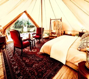 Acomodação em tenda com uma cama, cadeiras vermelhas, uma mesa e vista para área verde.
