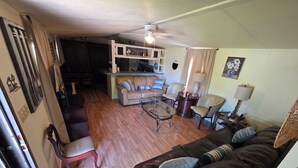 A living room with a leather sofa, a glass coffee table, and a beige sofa with striped pillows. There is a kitchen area with white cabinets and a ceiling fan. - Relax in this 2-bedroom lakefront home. Shared dock. Kayaks. Pet friendly (Cadiz)