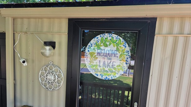 A door with a welcome sign, a security camera, and a decorative metal piece. - Relax in this 2-bedroom lakefront home. Shared dock. Kayaks. Pet friendly (Cadiz)