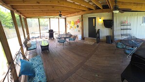 A covered outdoor patio with a wooden deck, metal furniture, a grill, and a wall-mounted TV. - Relax in this 2-bedroom lakefront home. Shared dock. Kayaks. Pet friendly (Cadiz)